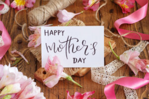 Happy Mother's Day card on a wooden table between pink flowers